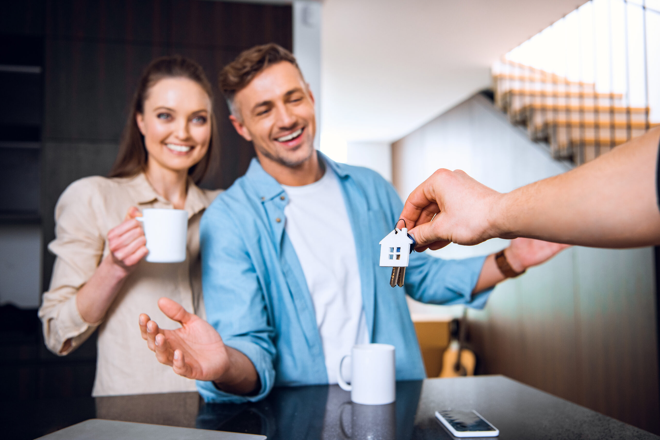 selective focus of man giving house shaped key chain to happy couple in new home