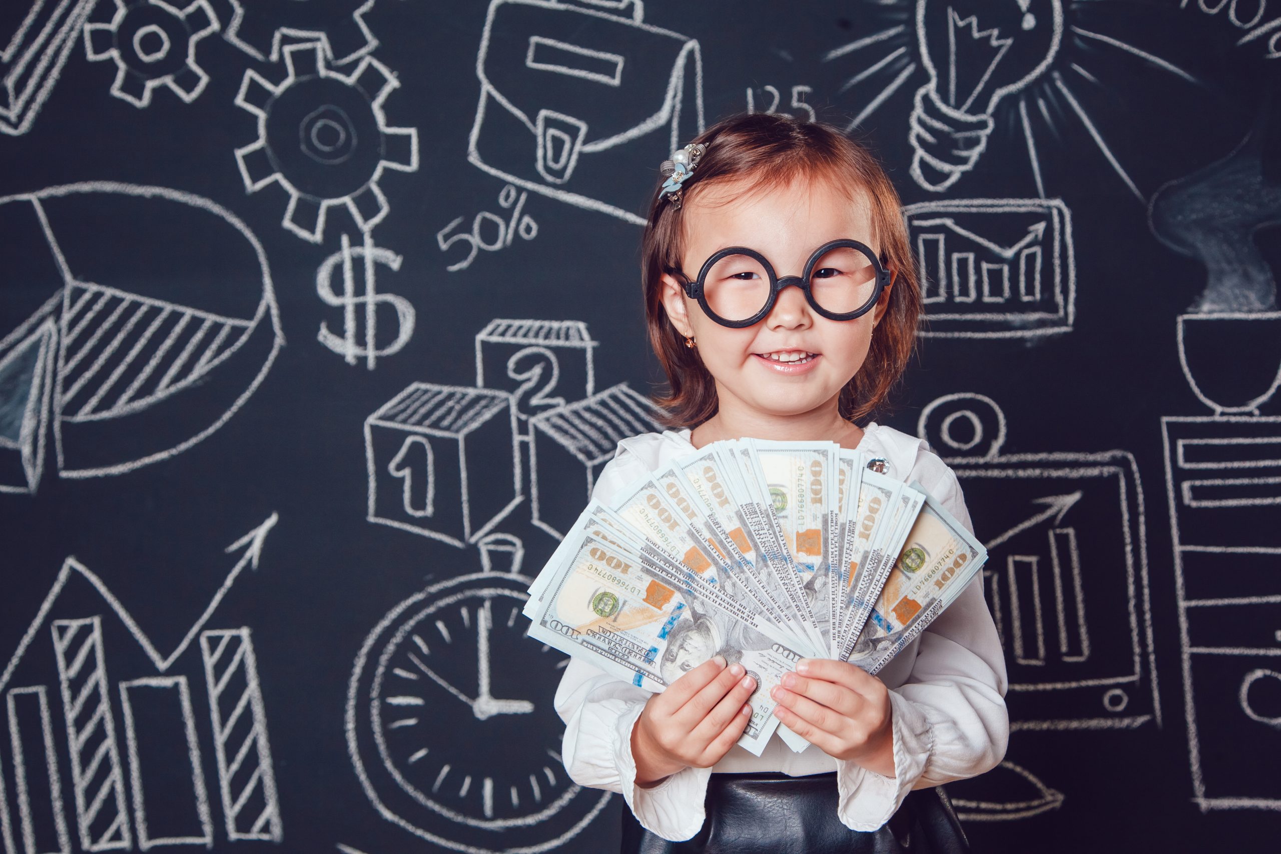 The little smart girl in glasses shows graphics company's business activity on a background of a wall with a picture