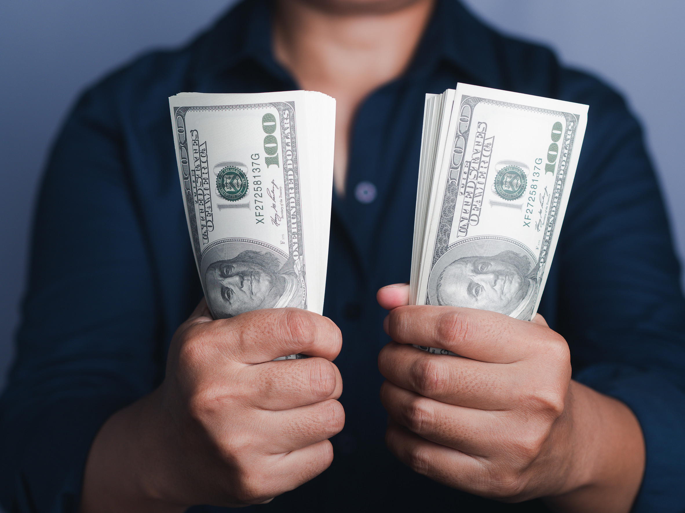 Hands holding of a US dollars banknote with a gray background while standing in the studio. Close-up photo. Space for text.