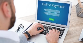 Man using laptop for online payment at wooden table, closeup